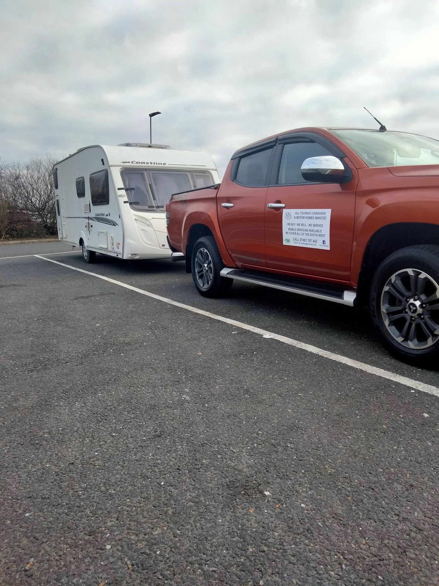 SJS Caravans' branded pickup — 'all touring caravans & motorhomes wanted' — towing a Coastline touring caravan